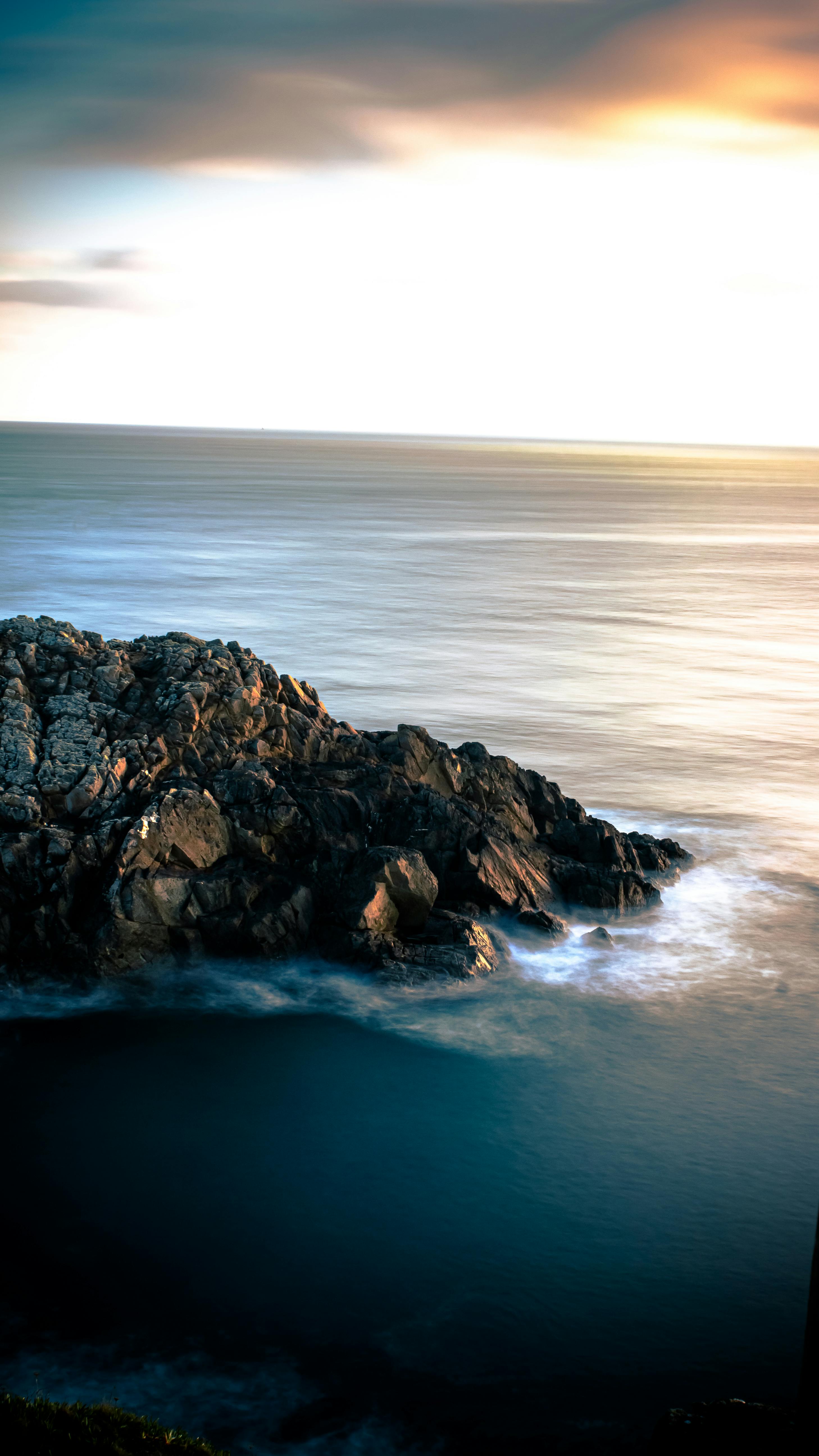 A Serene Sunset Over A Rocky Ocean Shoreline, Capturing The Tranquil Beauty Of Nature.