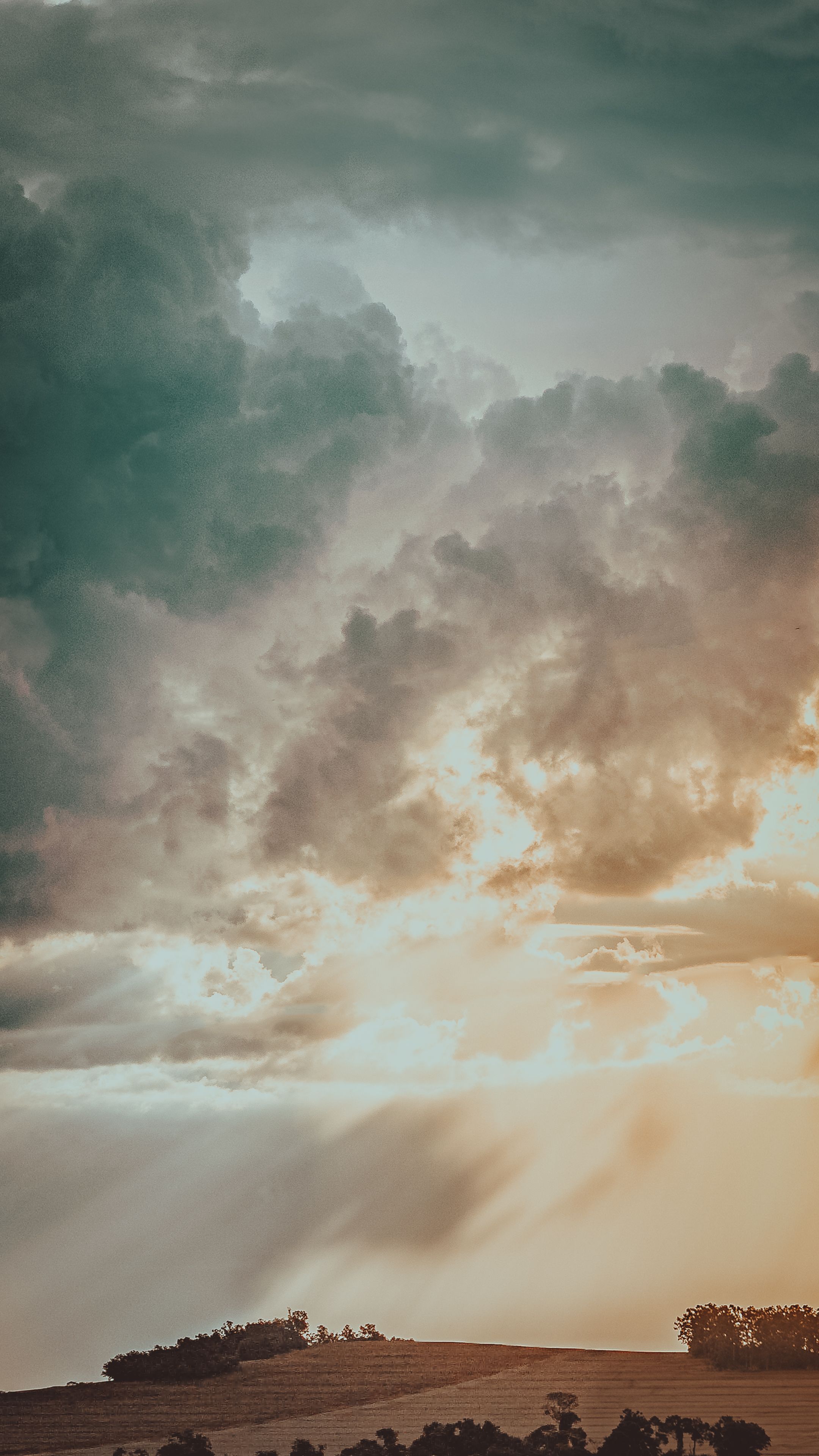 Captivating View Of Dramatic Clouds With Sunbeams Illuminating A Rural Hilltop Landscape.