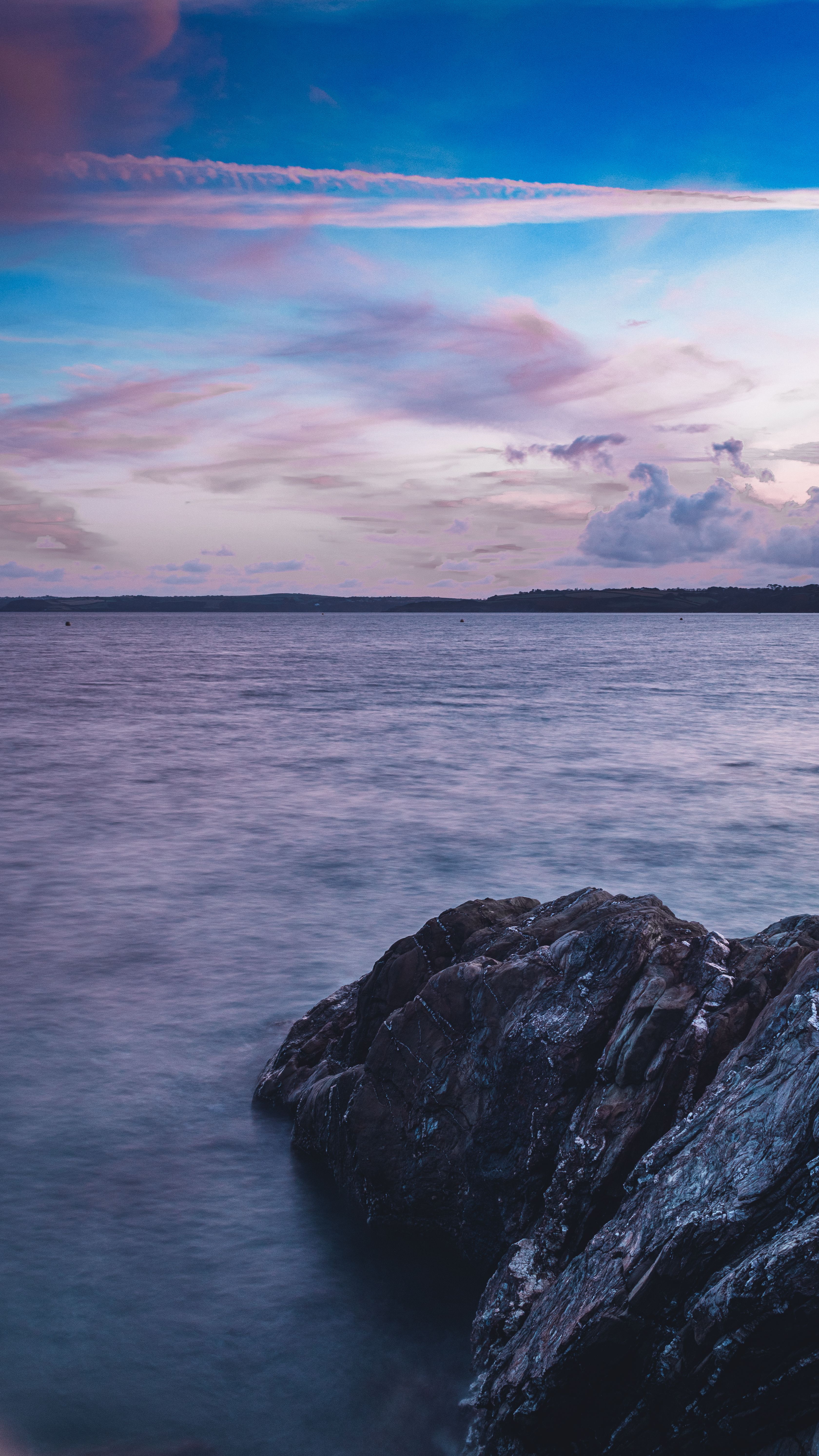 Serene Ocean And Rocky Shore At Dusk In Falmouth, England, With A Colorful Sky.