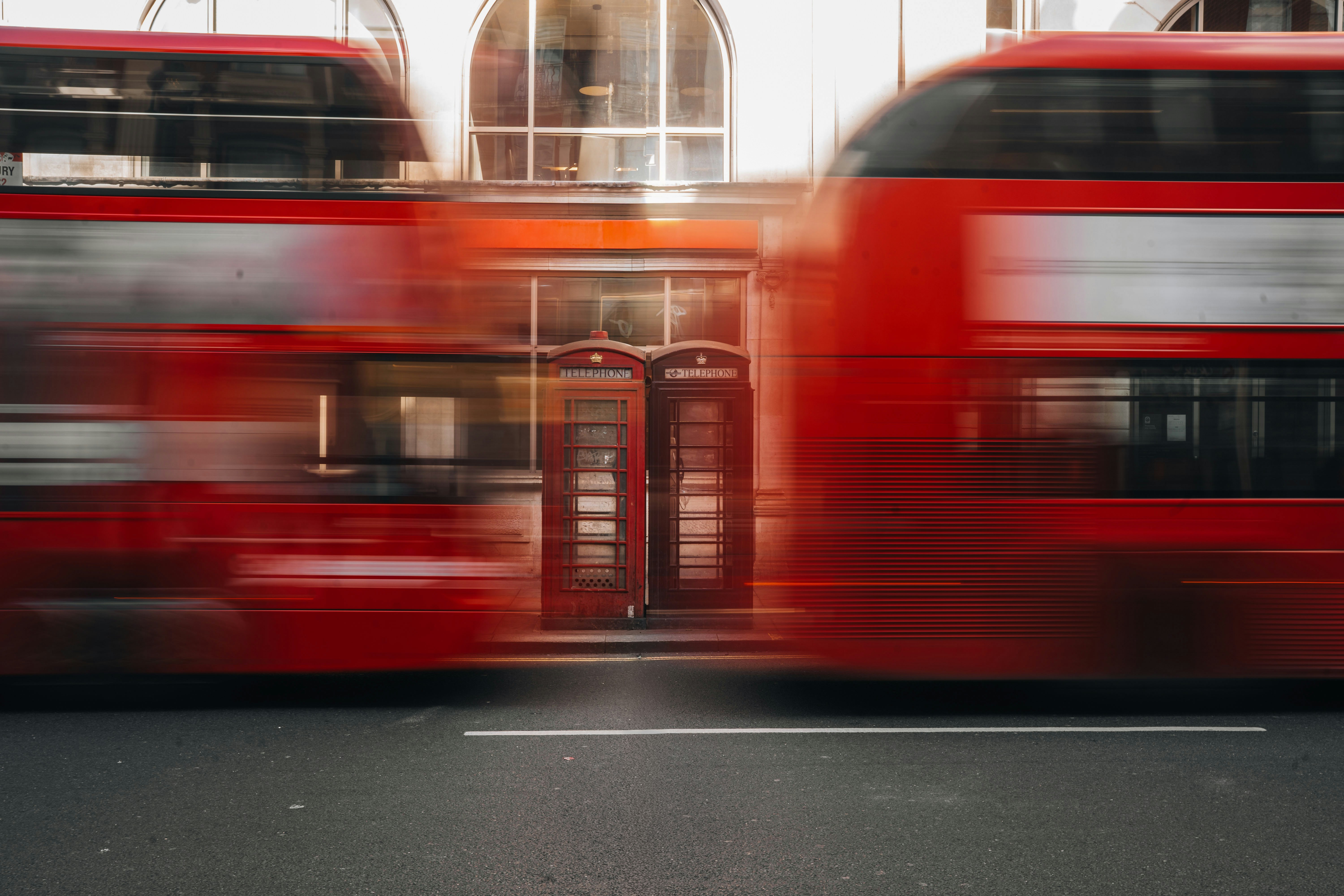 Two Blurred Red Double-decker Buses Passing A Building.