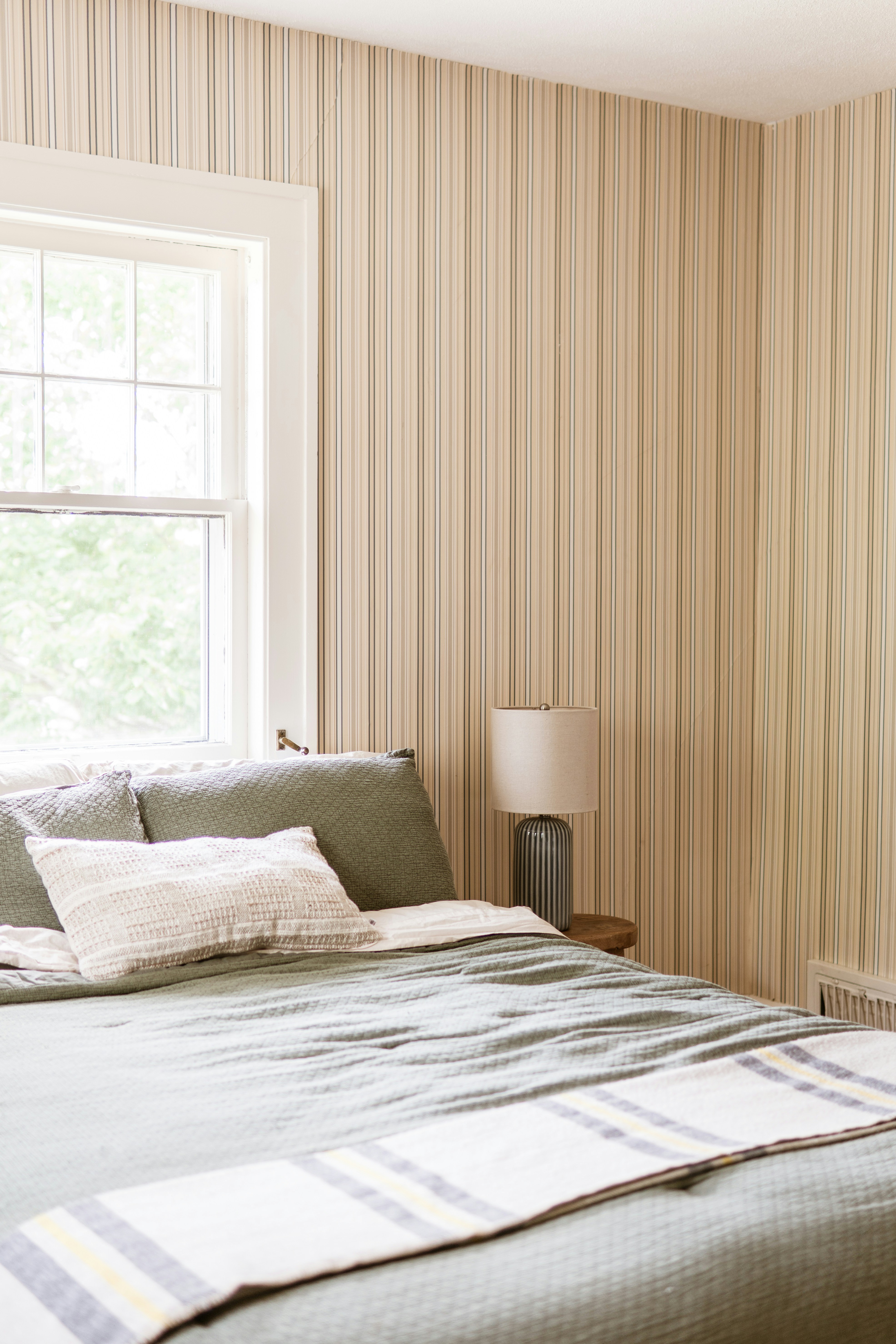 Cozy Bedroom With Green Bedding, Striped Wallpaper, And A Window.