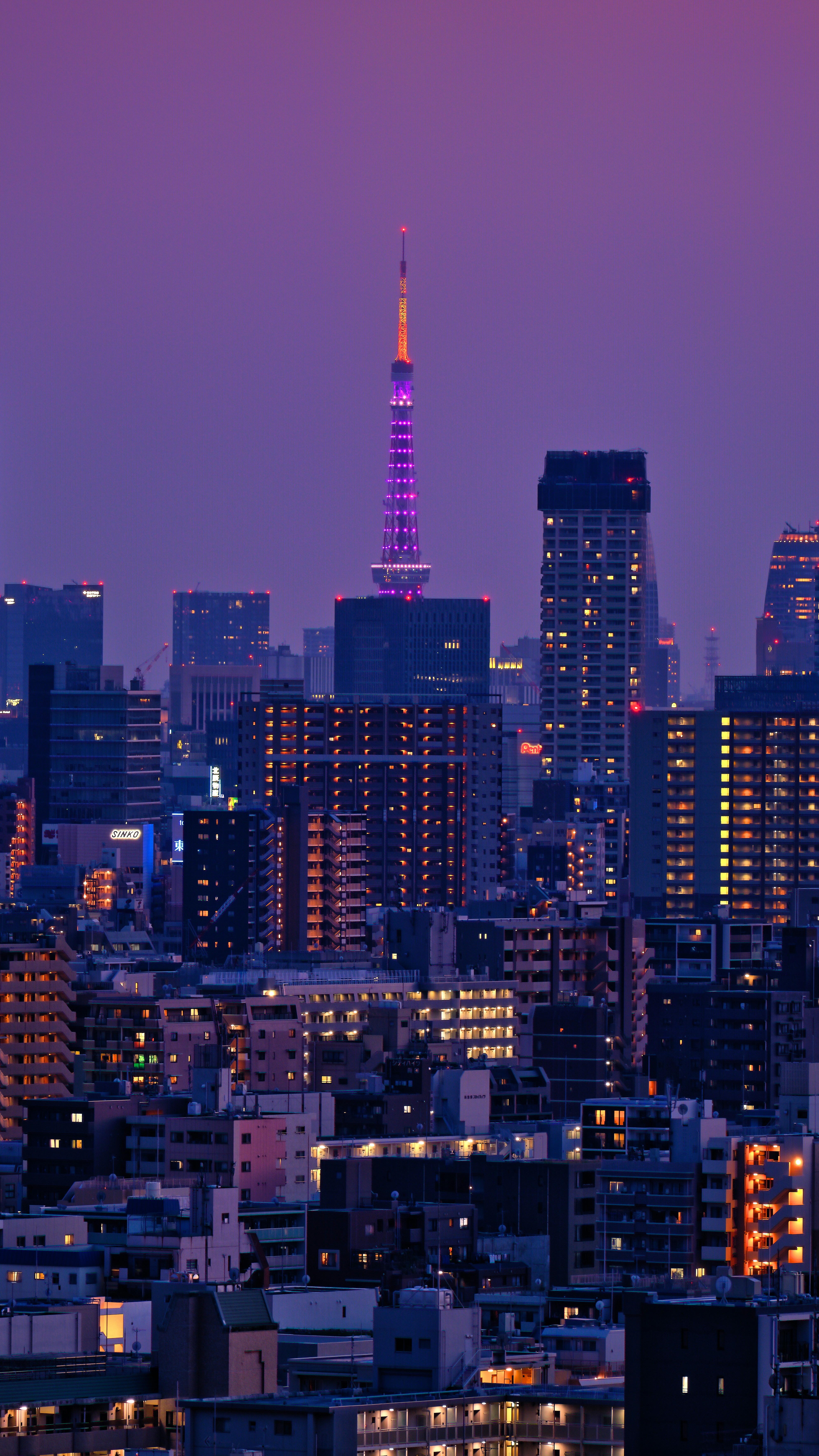 Illuminated City Skyline At Twilight With A Prominent Purple Tower.