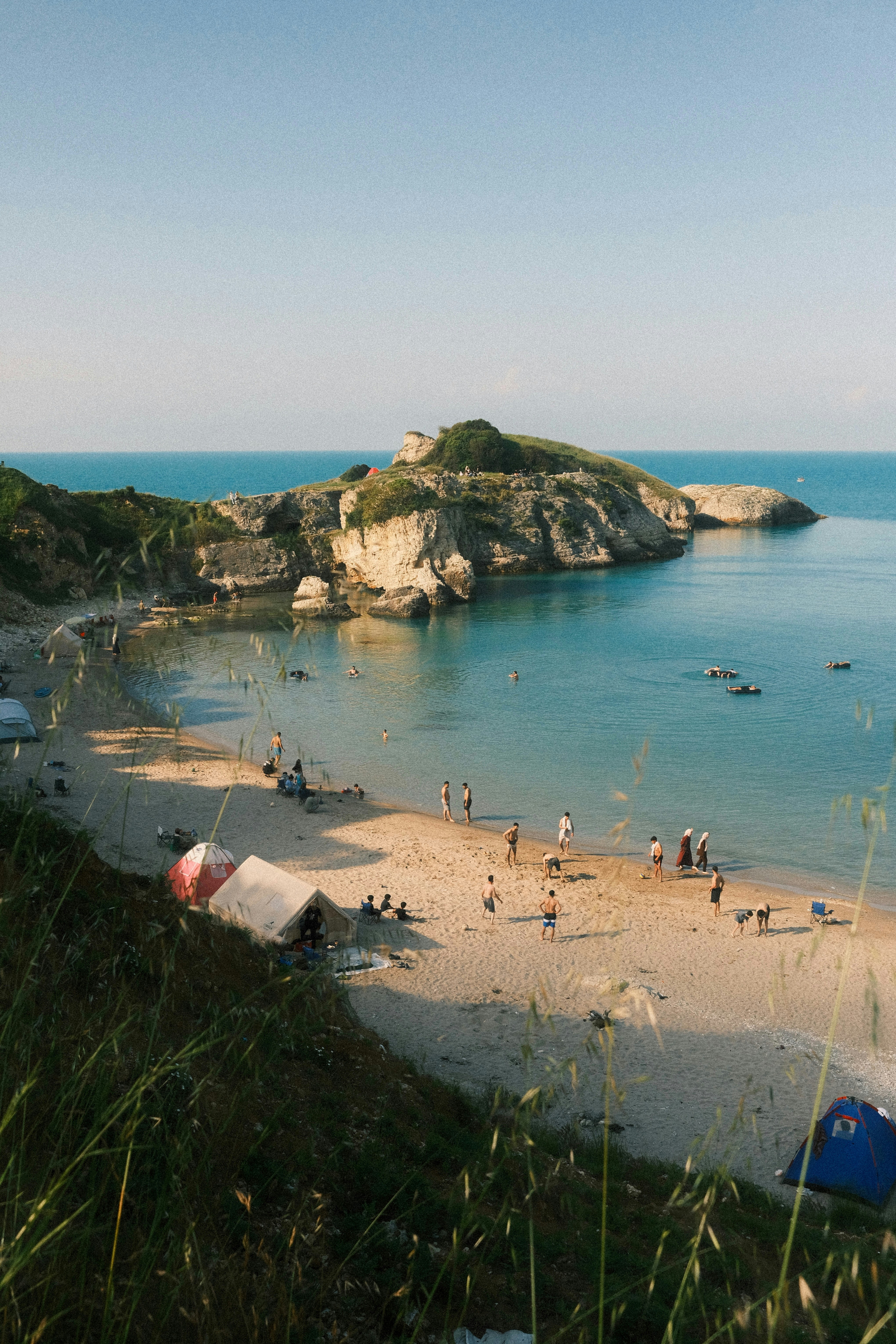 People Relaxing On A Sunny Beach With A Rocky Island.