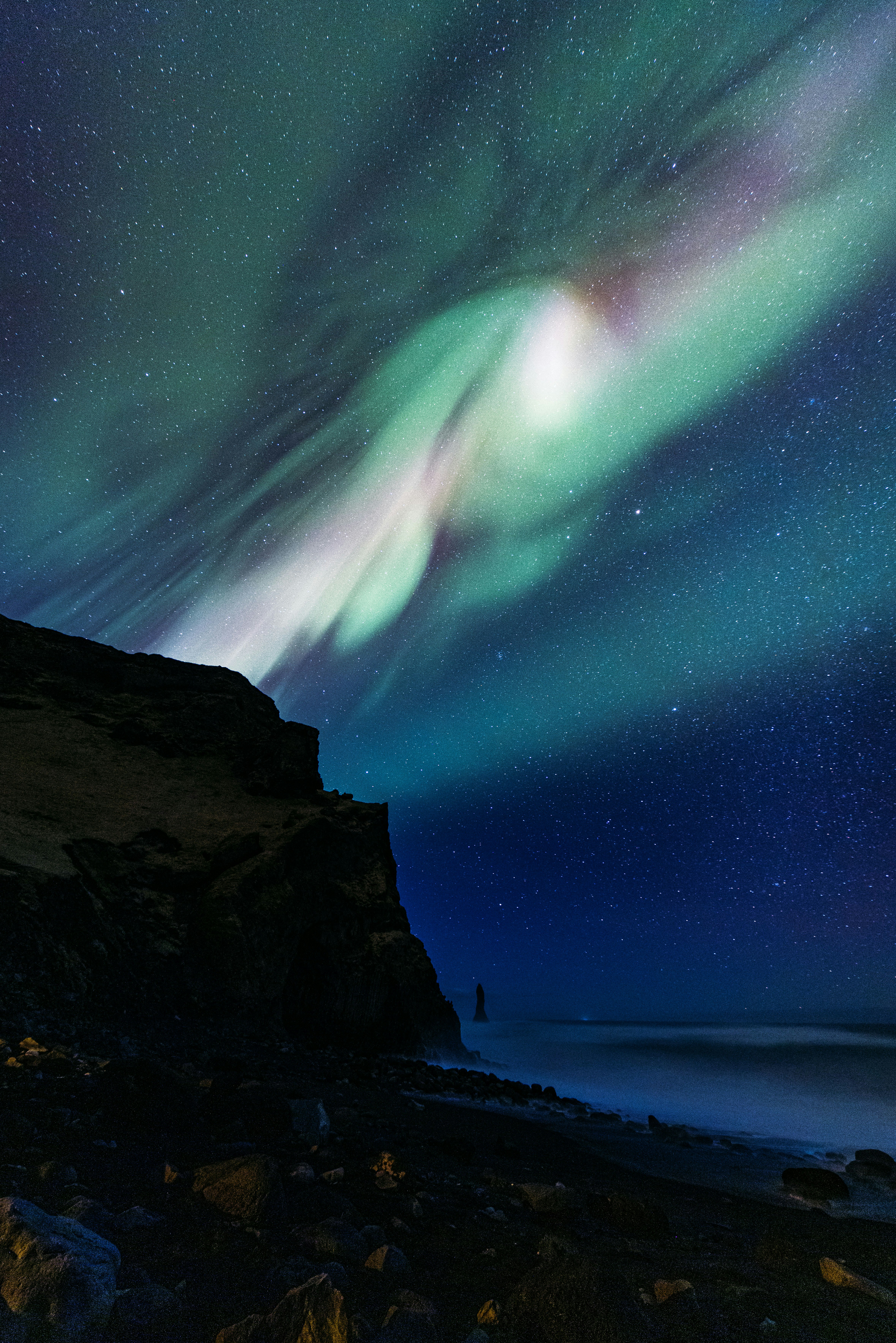 Aurora Borealis Illuminates Dark Night Sky Over Ocean And Cliffs.
