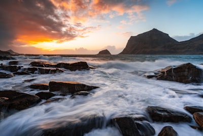 Vibrant Sunset Illuminates Ocean Waves Crashing On A Rocky Shore. wallpaper preview