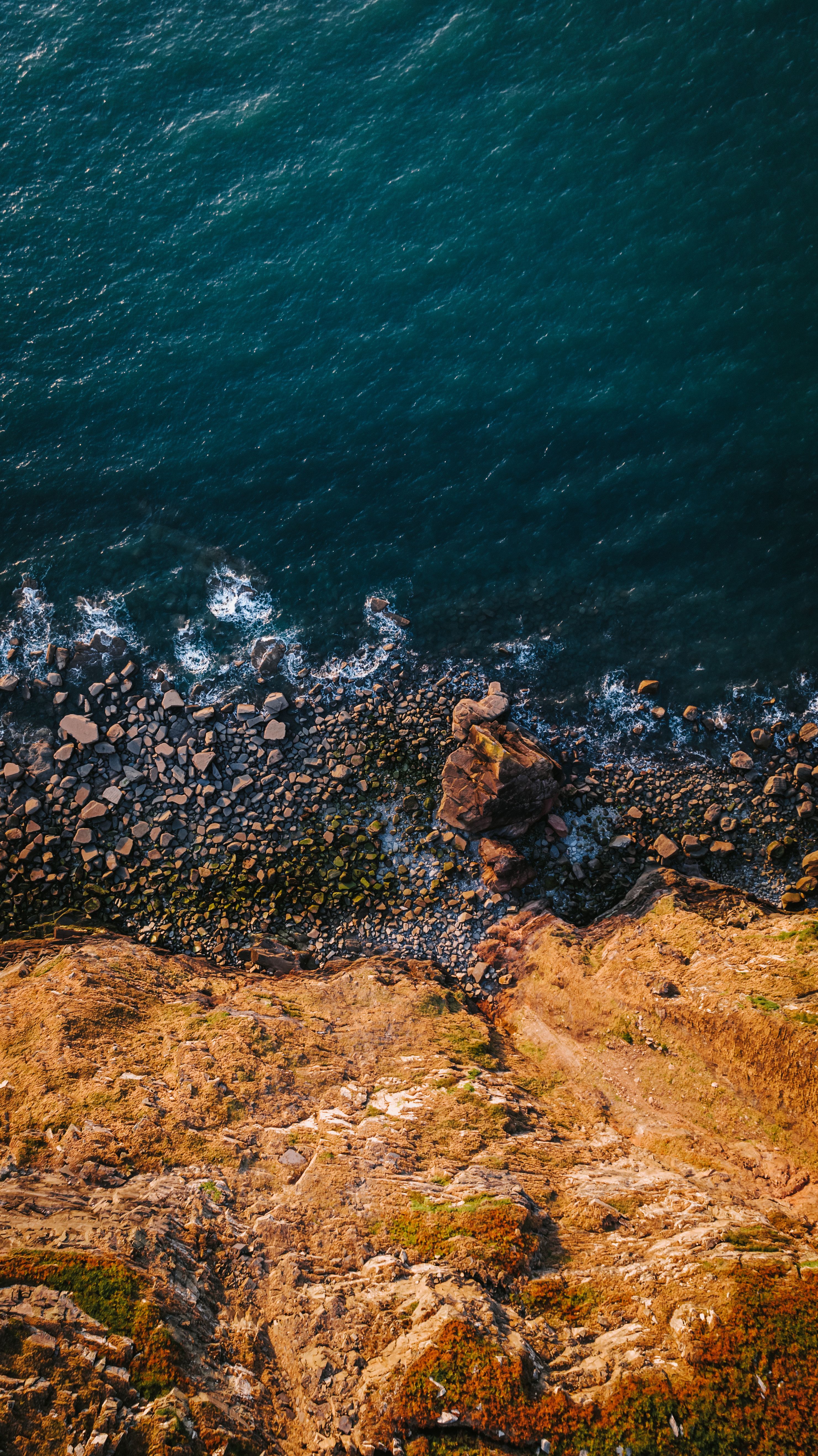 A Stunning Aerial View Of A Rocky Cliff Meeting The Ocean, Highlighting Nature's Beauty. HD mobile wallpaper