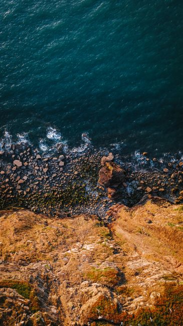 A Stunning Aerial View Of A Rocky Cliff Meeting The Ocean, Highlighting Nature's Beauty. wallpaper preview