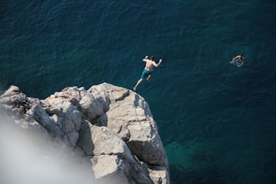 Man Cliff Diving Into Clear Blue Ocean Water.