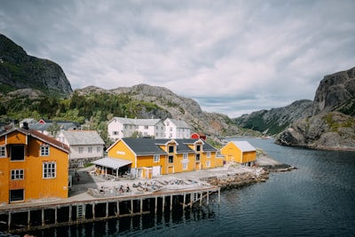 The Colorful Waterfront Of Nusfjord Rests Between Steep Granite Mountains And Calm Arctic Waters. This Scenic View Captures One Of Norway’s Best-preserved Fishing Villages, Blending Traditional Architecture With The Rugged Beauty Of The Lofoten Islands.