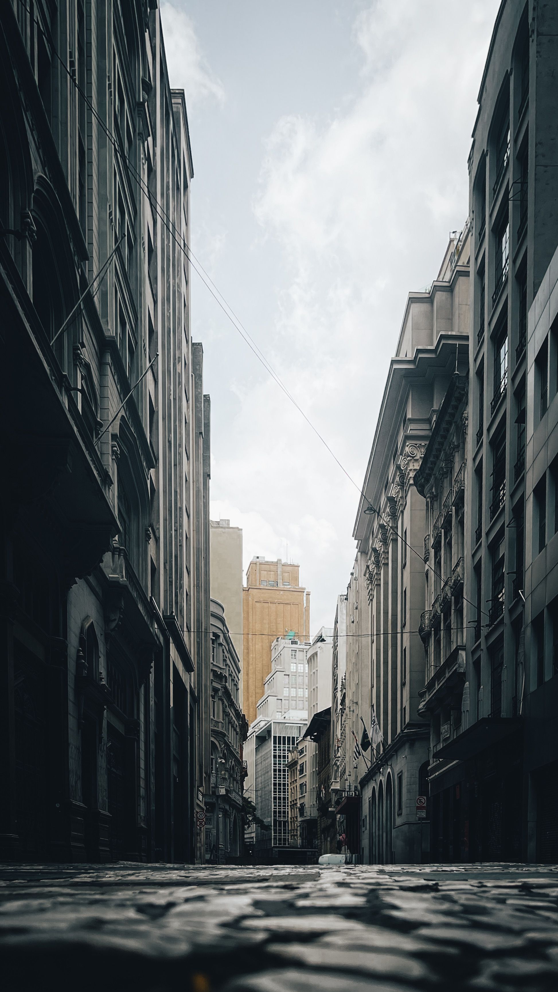 A Serene Urban Alleyway Framed By Tall Buildings Under A Cloudy Sky, Showcasing Architectural Beauty. HD mobile wallpaper