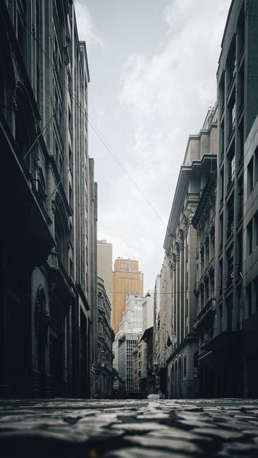 A Serene Urban Alleyway Framed By Tall Buildings Under A Cloudy Sky, Showcasing Architectural Beauty. wallpaper preview