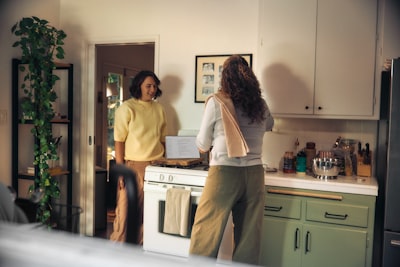 Two Women Talking In A Kitchen While Cooking wallpaper preview