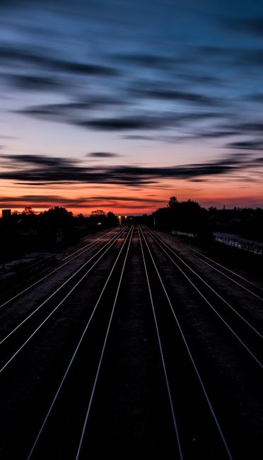 Long Railway Tracks Stretching Into The Horizon Under A Dramatic Twilight Sky.