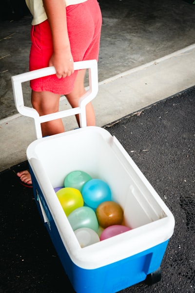 A Child Pulls A Cooler Filled With Colorful Water Balloons.