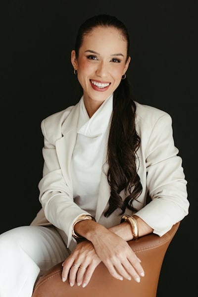 Smiling Woman In White Blazer Sitting In A Chair.