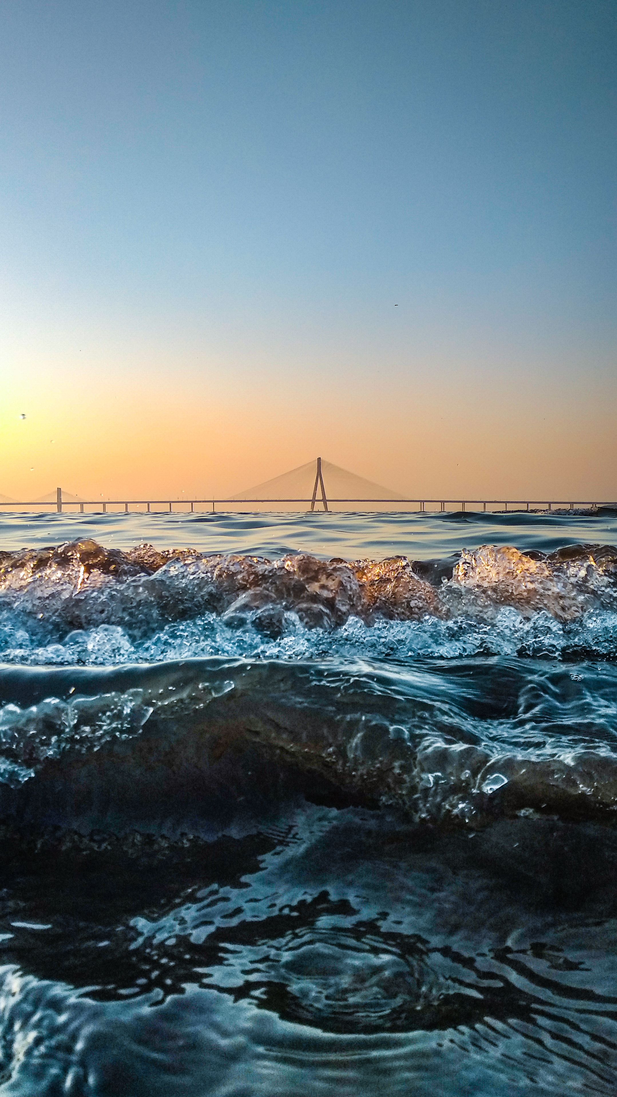 Dramatic Ocean Waves Crashing At Sunset With A Beautiful Bridge In The Distance. HD mobile wallpaper