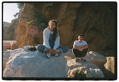 Two People Sitting On Rocks Near The Ocean.