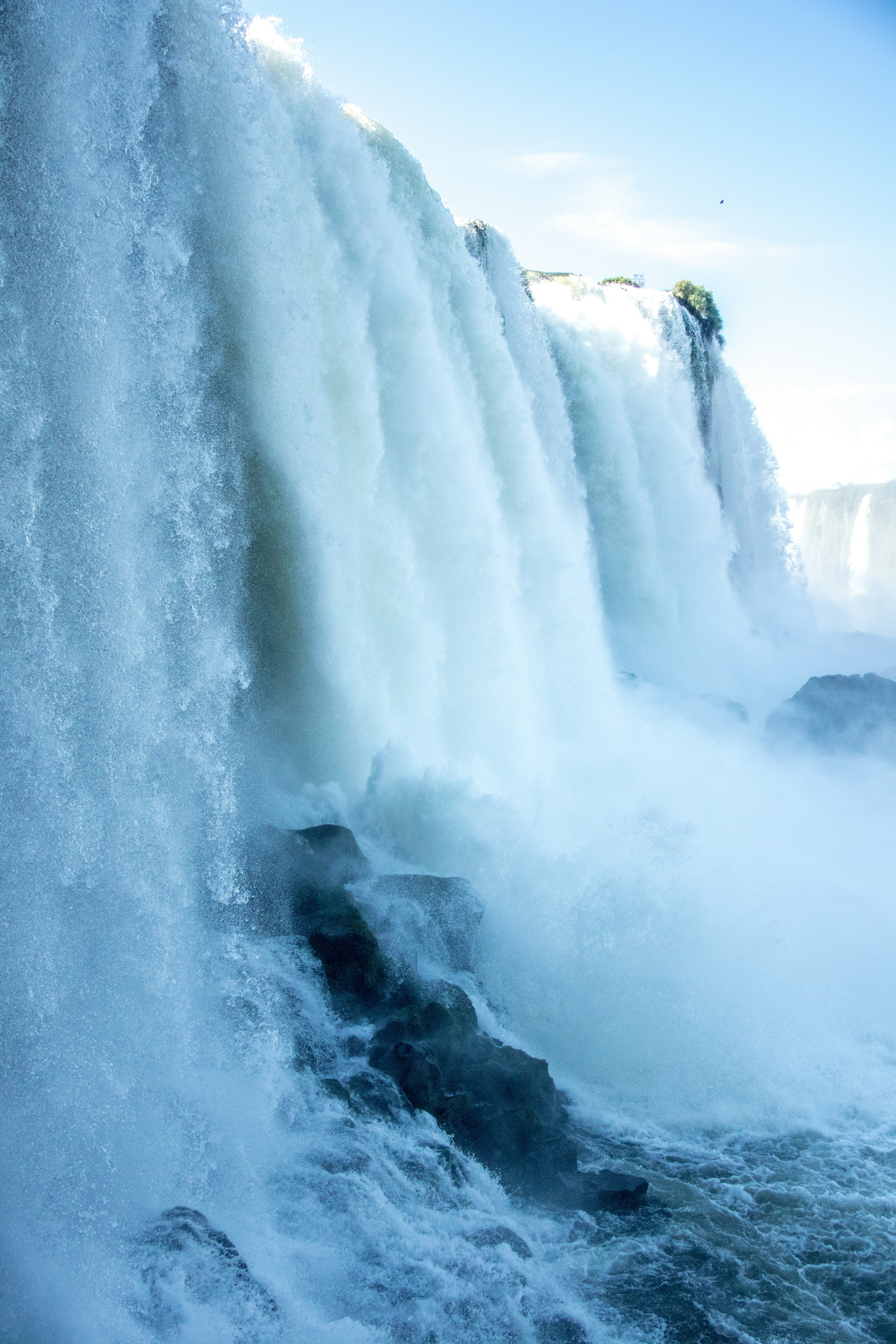 A Powerful Waterfall Cascades Over Rocks Under A Bright Sky. HD mobile wallpaper