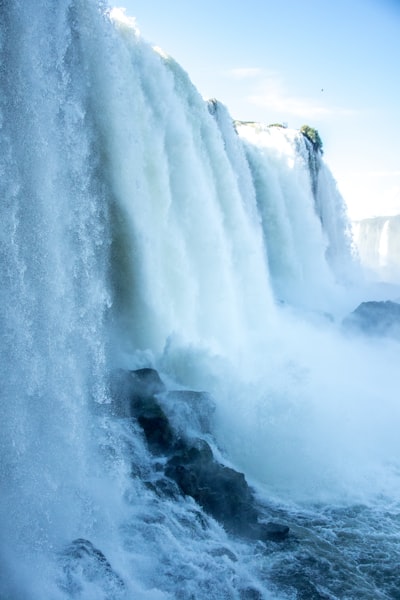 A Powerful Waterfall Cascades Over Rocks Under A Bright Sky.