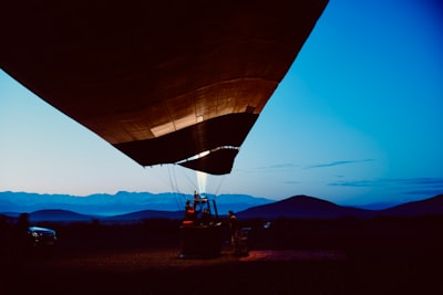 Hot Air Balloon Inflation At Twilight Over Mountains.