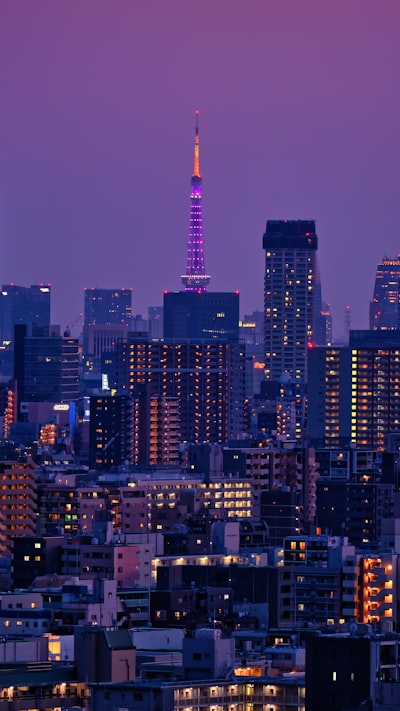Illuminated City Skyline At Twilight With A Prominent Purple Tower. wallpaper preview