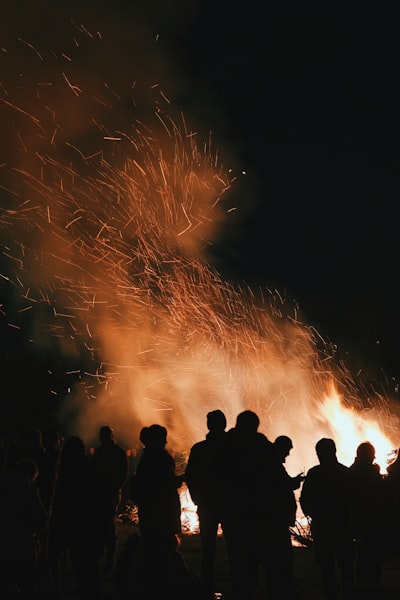 Silhouettes Of People Gathered Around A Large Bonfire At Night.