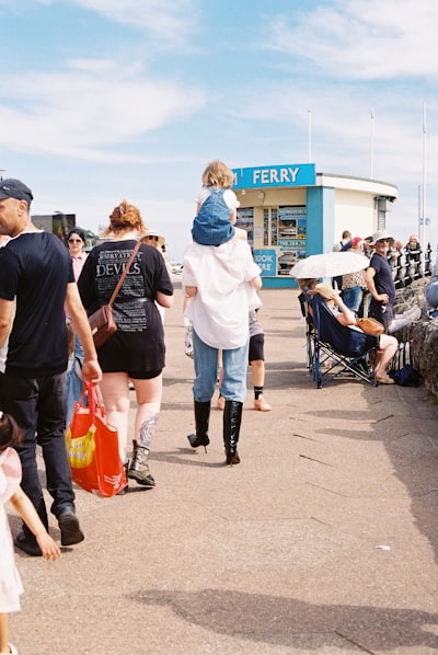 Child On Shoulders Walks Past A Ferry Booth.