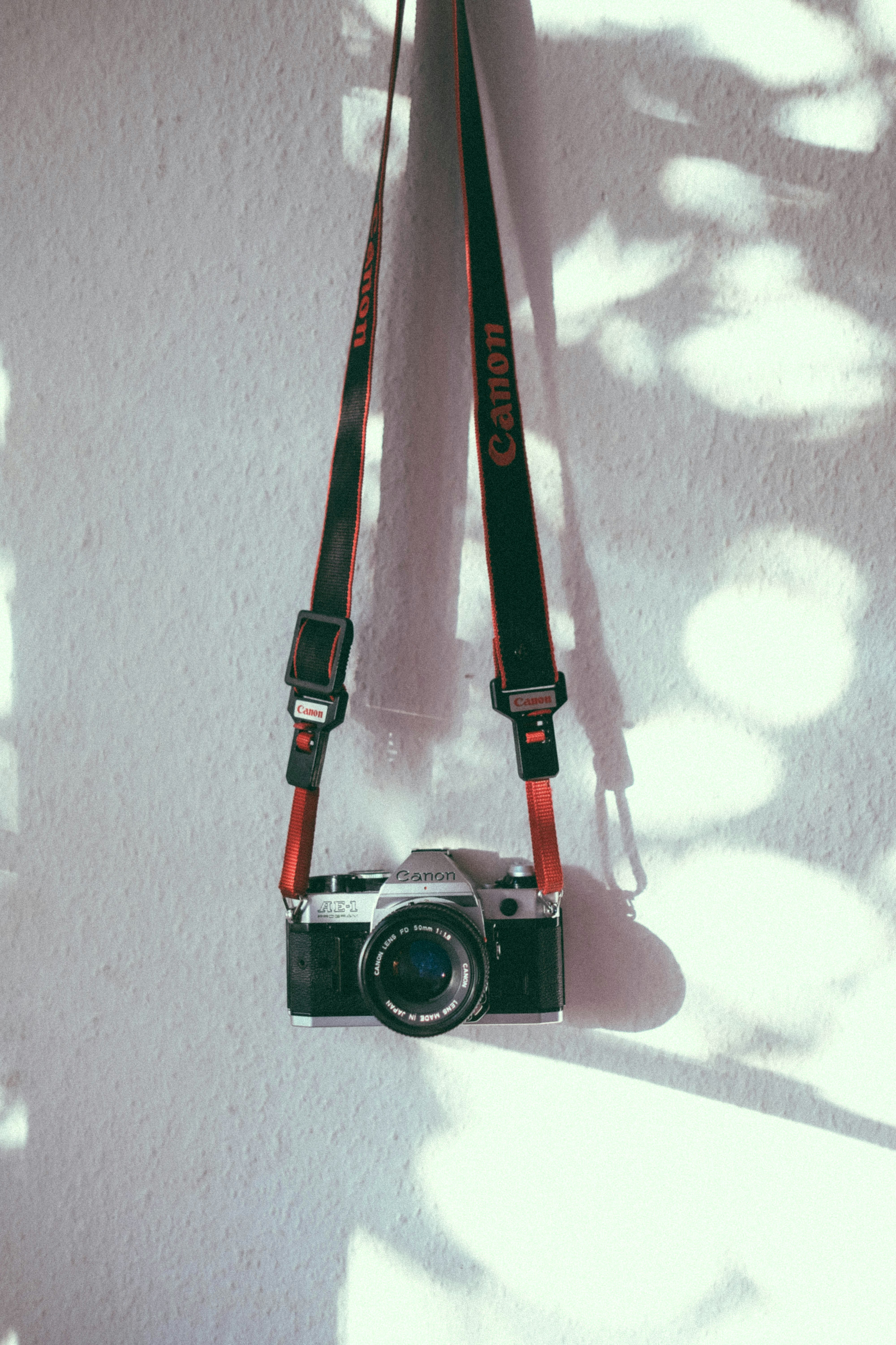 Vintage Canon Film Camera Hanging Against A Sunlit White Wall. HD mobile wallpaper