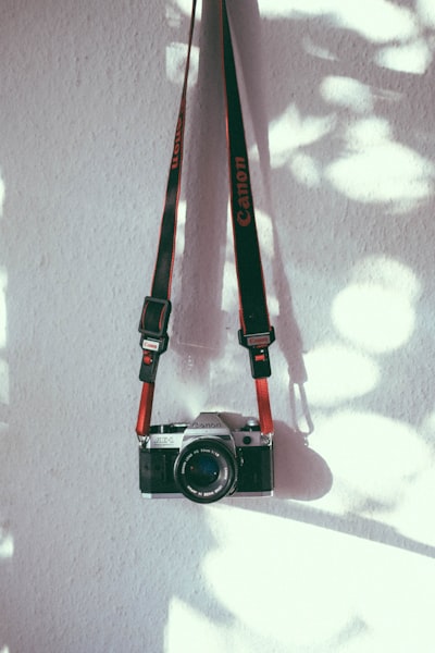 Vintage Canon Film Camera Hanging Against A Sunlit White Wall. wallpaper preview