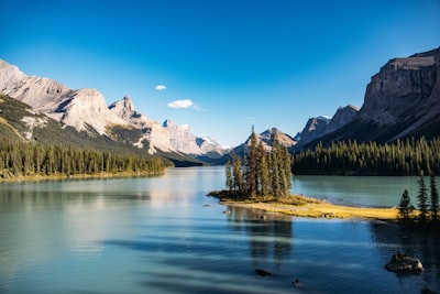 Serene Lake With A Tree-covered Island, Surrounded By Majestic Mountains.