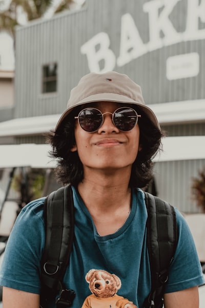Young Man In Hat And Sunglasses Smiling Near A Bakery.