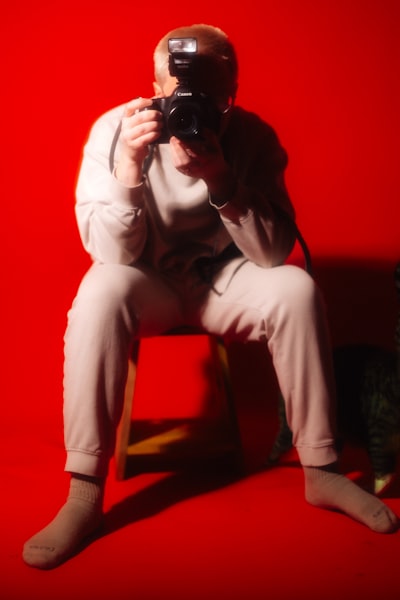 Person With Camera Takes A Photo Against Red Background.
