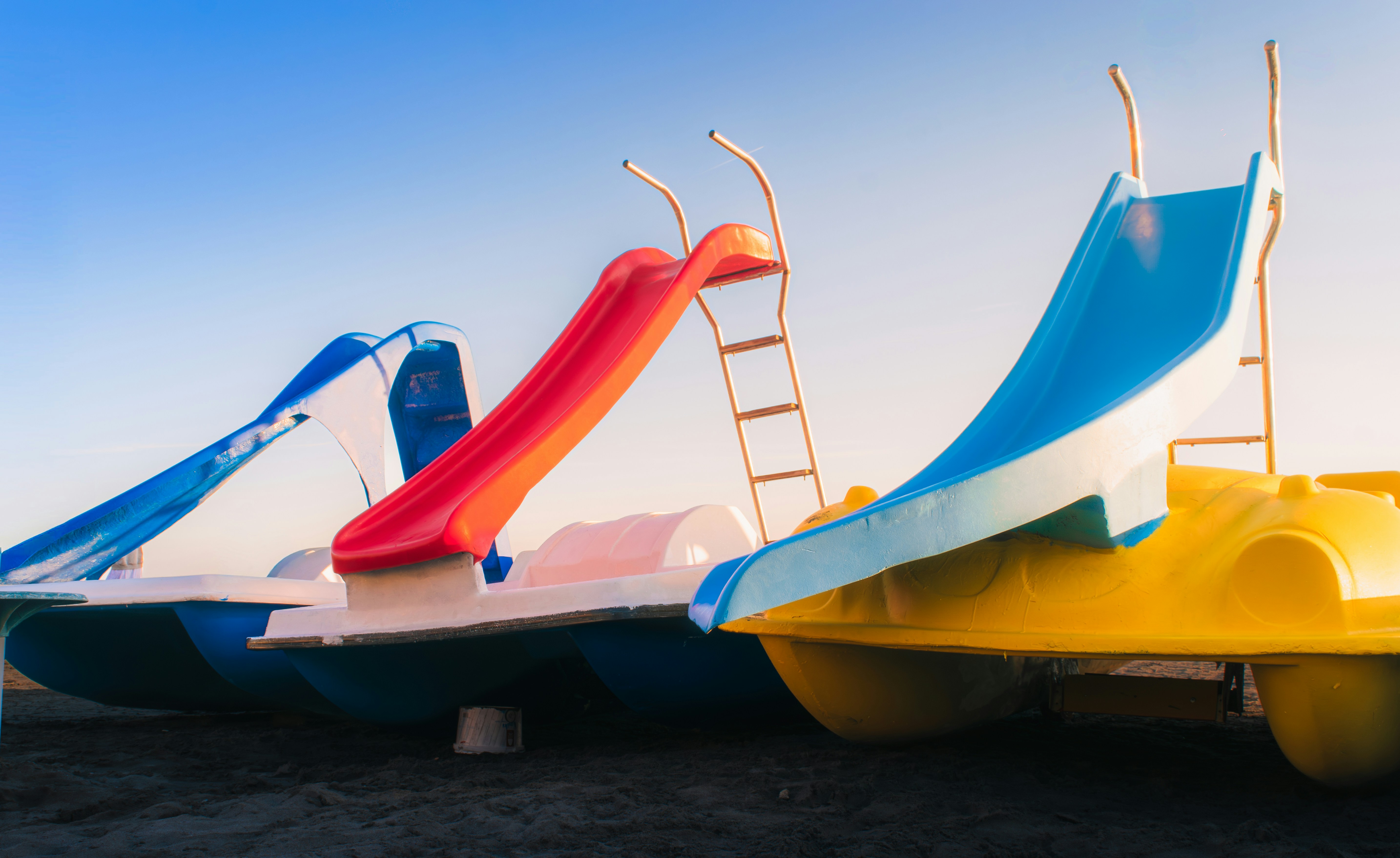 Three Colorful Pedal Boats With Slides Under A Clear Sky. HD mobile wallpaper