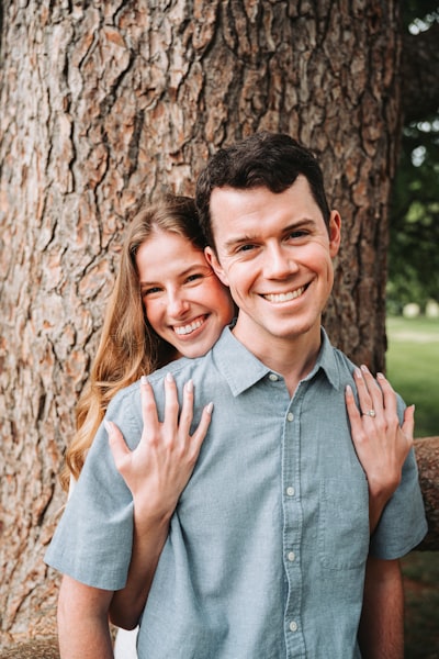 A Smiling Couple Embraces In Front Of A Tree.