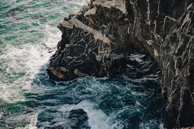 Dark, Rugged Cliffs Meet Foamy, Turbulent Ocean Water.