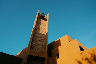Angular Earth-toned Building With A Prominent Tower Against Blue Sky.