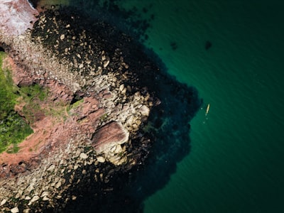 A Single Yellow Kayak Tracing The Coast Along The Shallows Of Babbacombe, Devon, UK