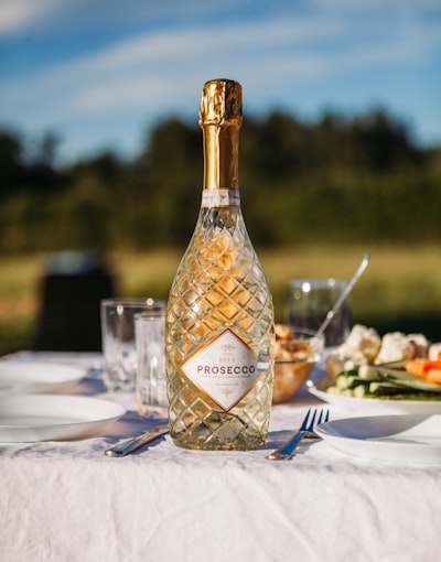 A Bottle Of Prosecco On A White Table Outdoors.