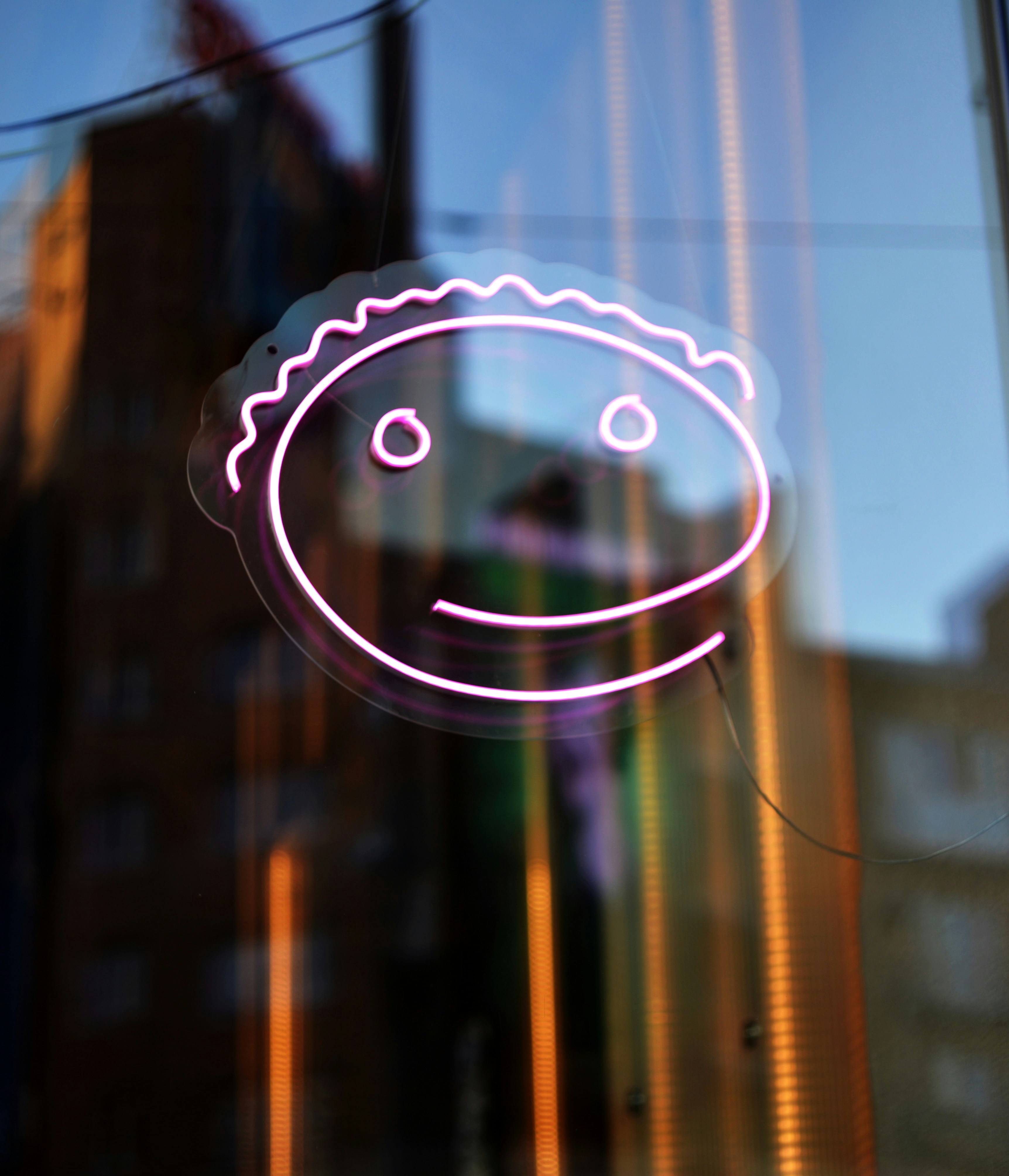 A Pink Neon Smiling Face Sign On A Reflective Window. HD mobile wallpaper