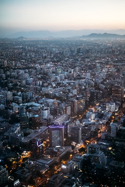 Panoramic City View At Twilight With Illuminated Buildings And Mountains.