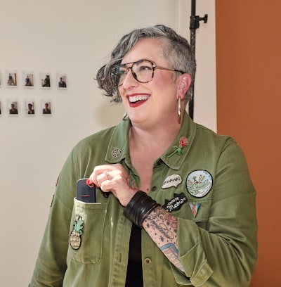 Smiling Woman Puts Device Into Her Patched Olive Green Jacket. wallpaper preview